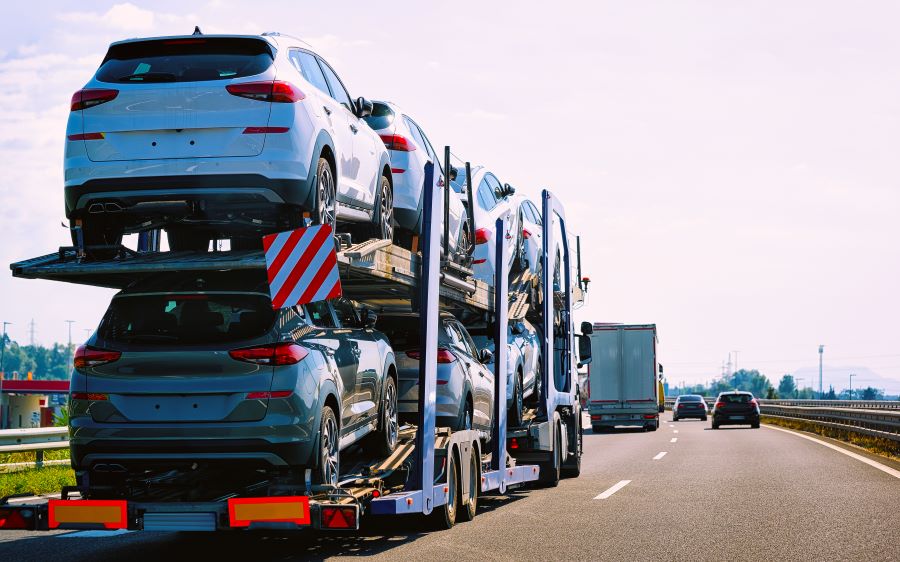 uma carreta transportando vários carros novos em uma rodovia. A carreta é carregada com carros de cores principalmente cinza e branco, todos arrumados em dois níveis