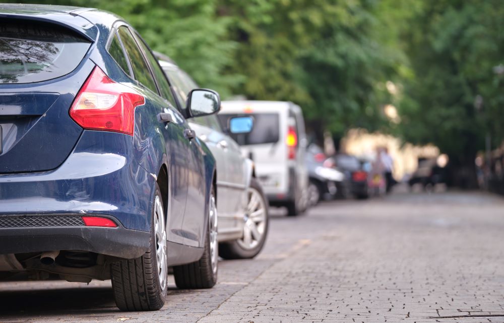 Carros estacionados ao longo de uma rua arborizada, com destaque para um veículo azul em primeiro plano, representando a atmosfera urbana típica de modelos de carros até 60 mil reais.
