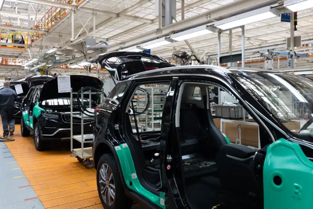 carros chineses no brasil: Linha de produção em fábrica de automóveis, com carros em montagem e portas abertas, mostrando o interior da planta industrial e veículos prontos para inspeção e acabamento