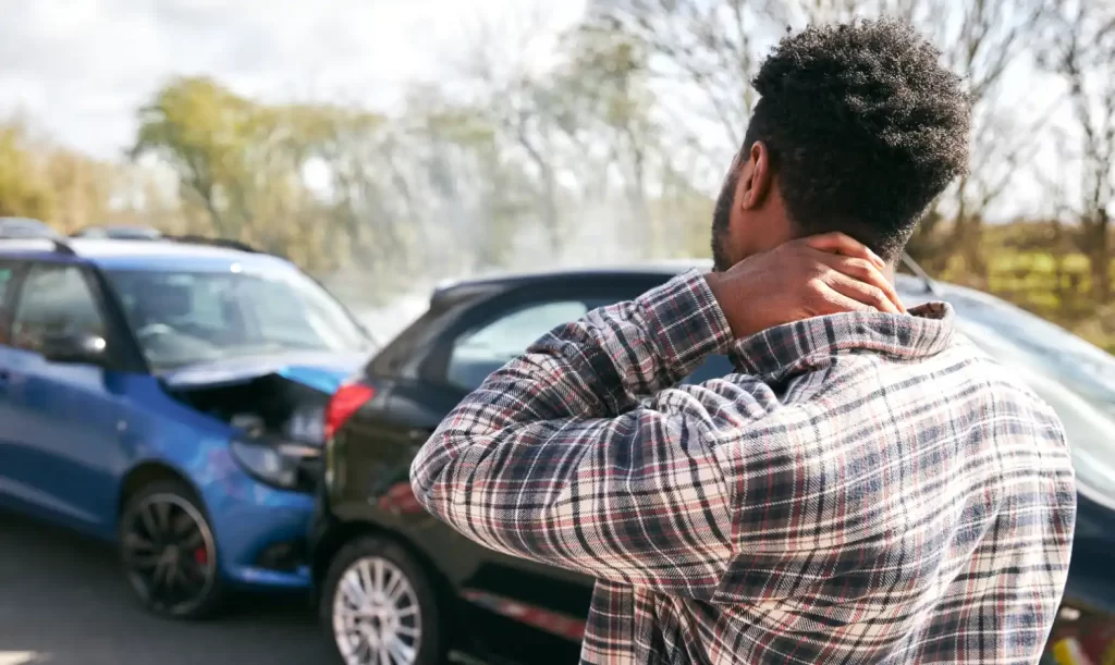 Homem com as mãos no rosto, aborrecido ao lado de carros estacionados, sugerindo preocupação com problemas no veículo. como saber se o carro tem sinistro